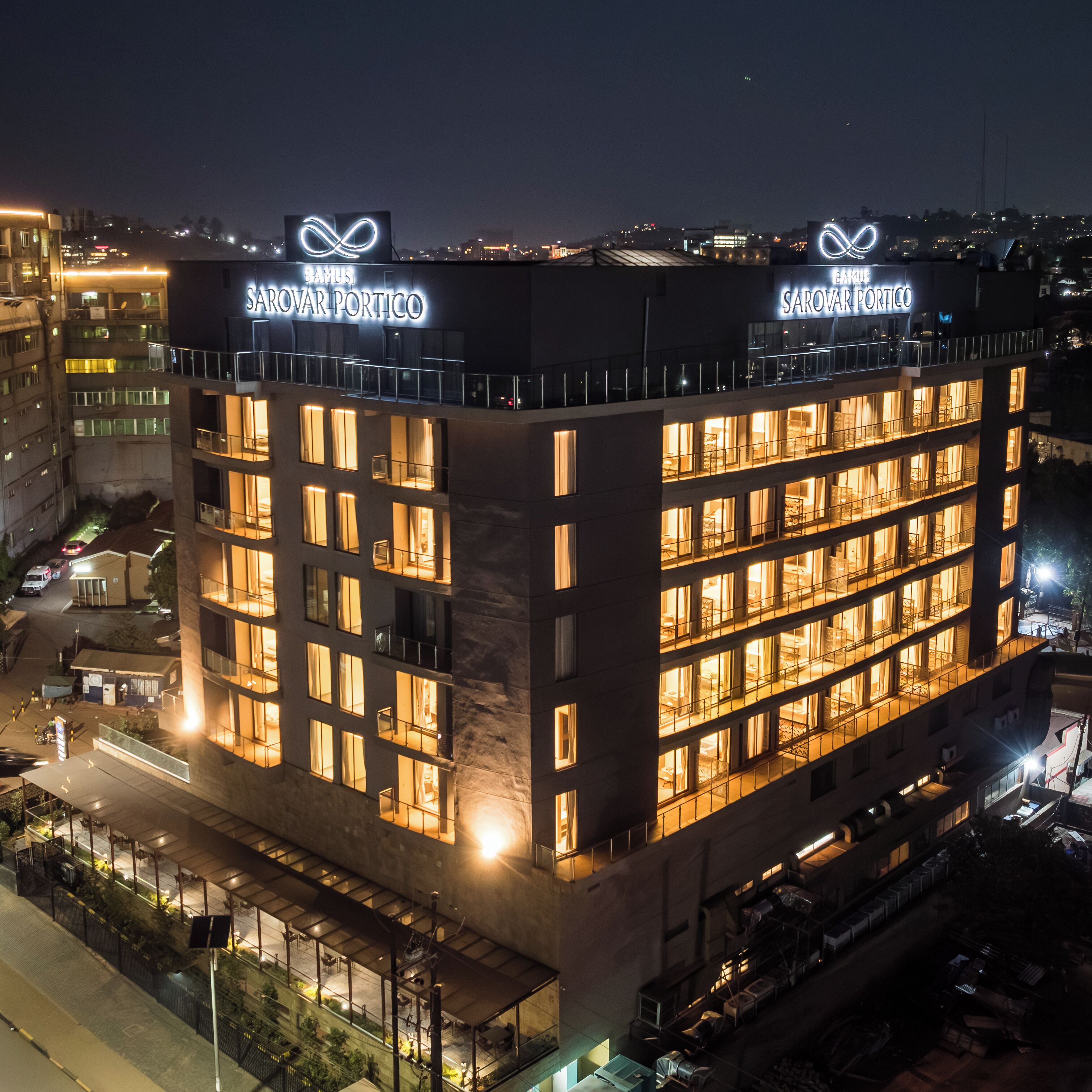 A multi-story hotel with illuminated windows and balconies, a prominent infinity sign logo, and a view of the surrounding cityscape.