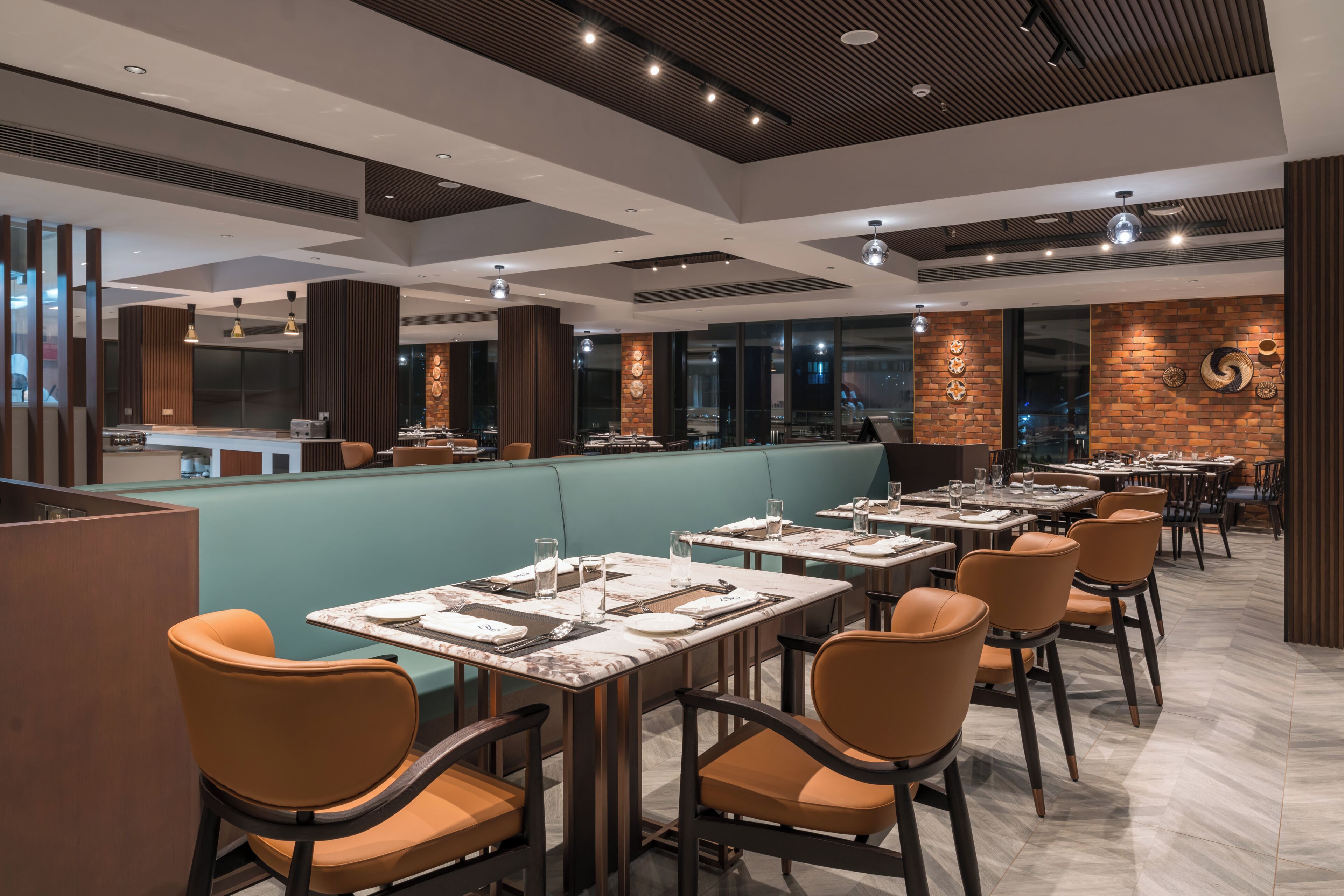 A modern restaurant with a long counter, booths, and a brick accent wall.