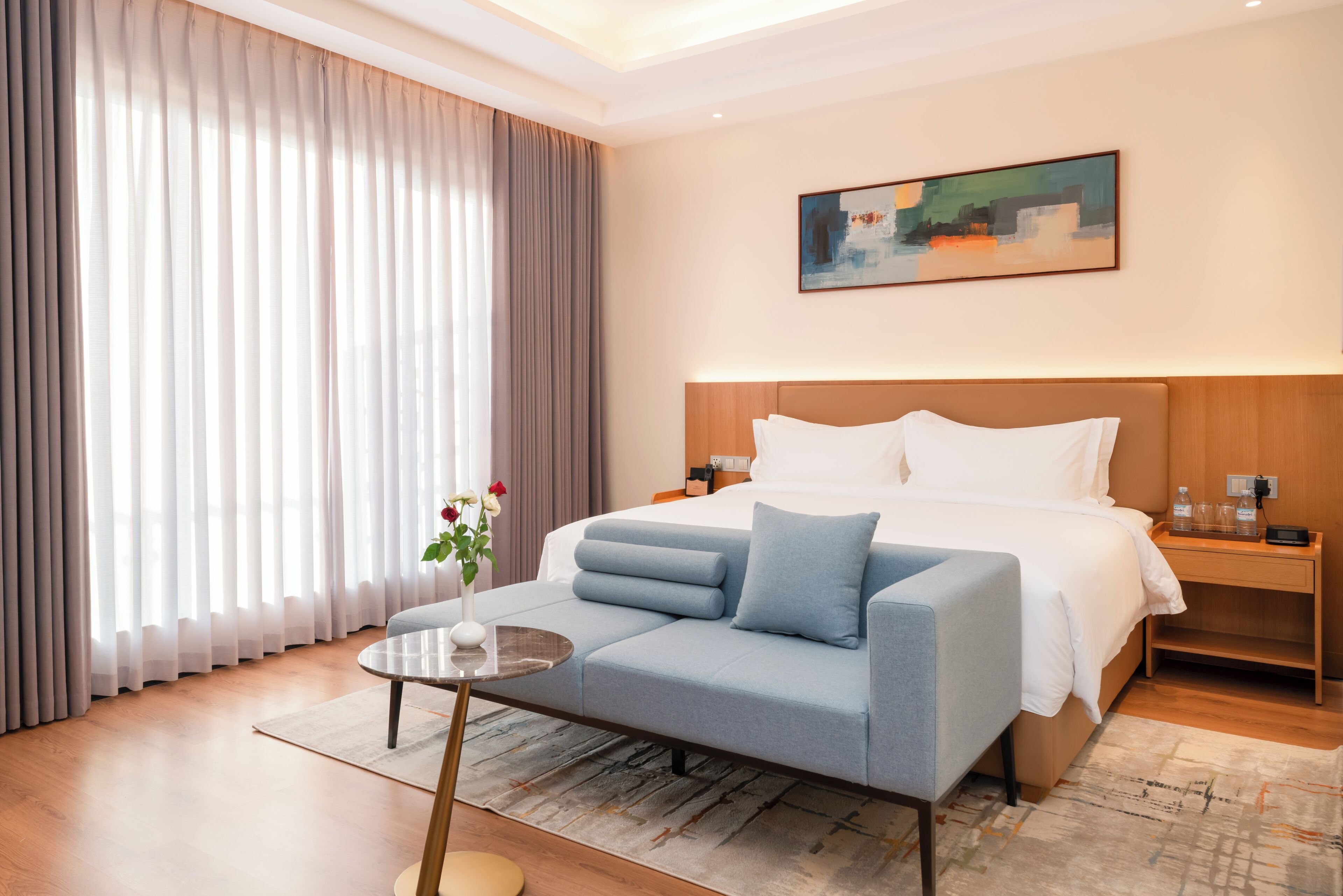 A hotel room with a bed, a sofa, a small table, and a painting on the wall.