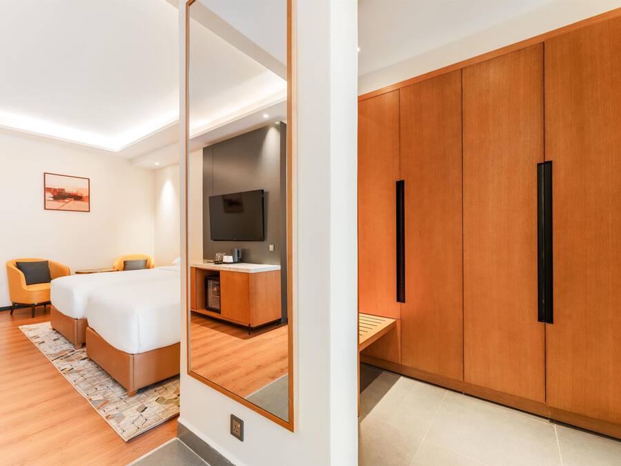 Una habitación de hotel moderna con una cama, dos sillas, un televisor, un armario de madera y un espejo.