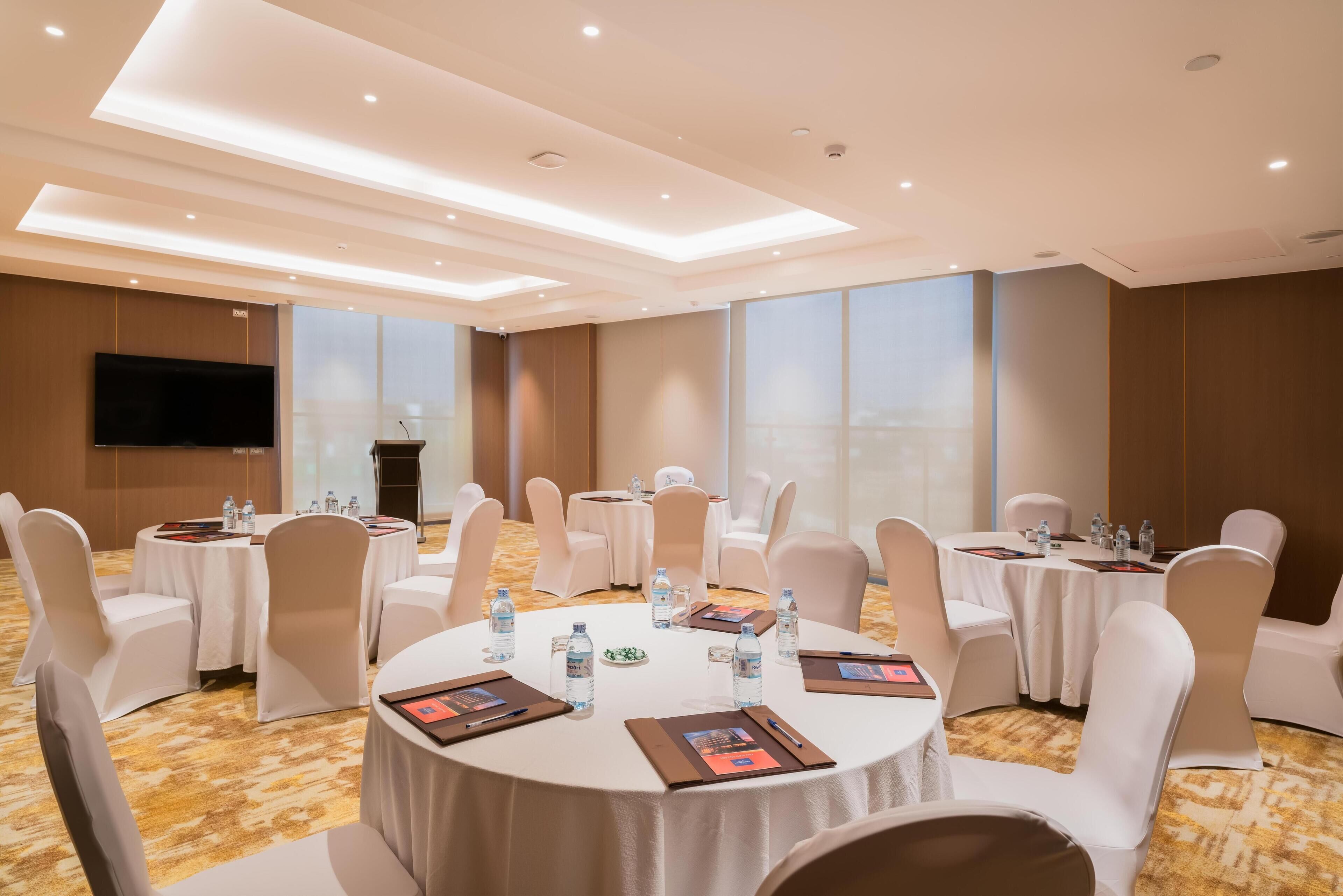 A conference room with round tables, white chairs, and a flat-screen TV.