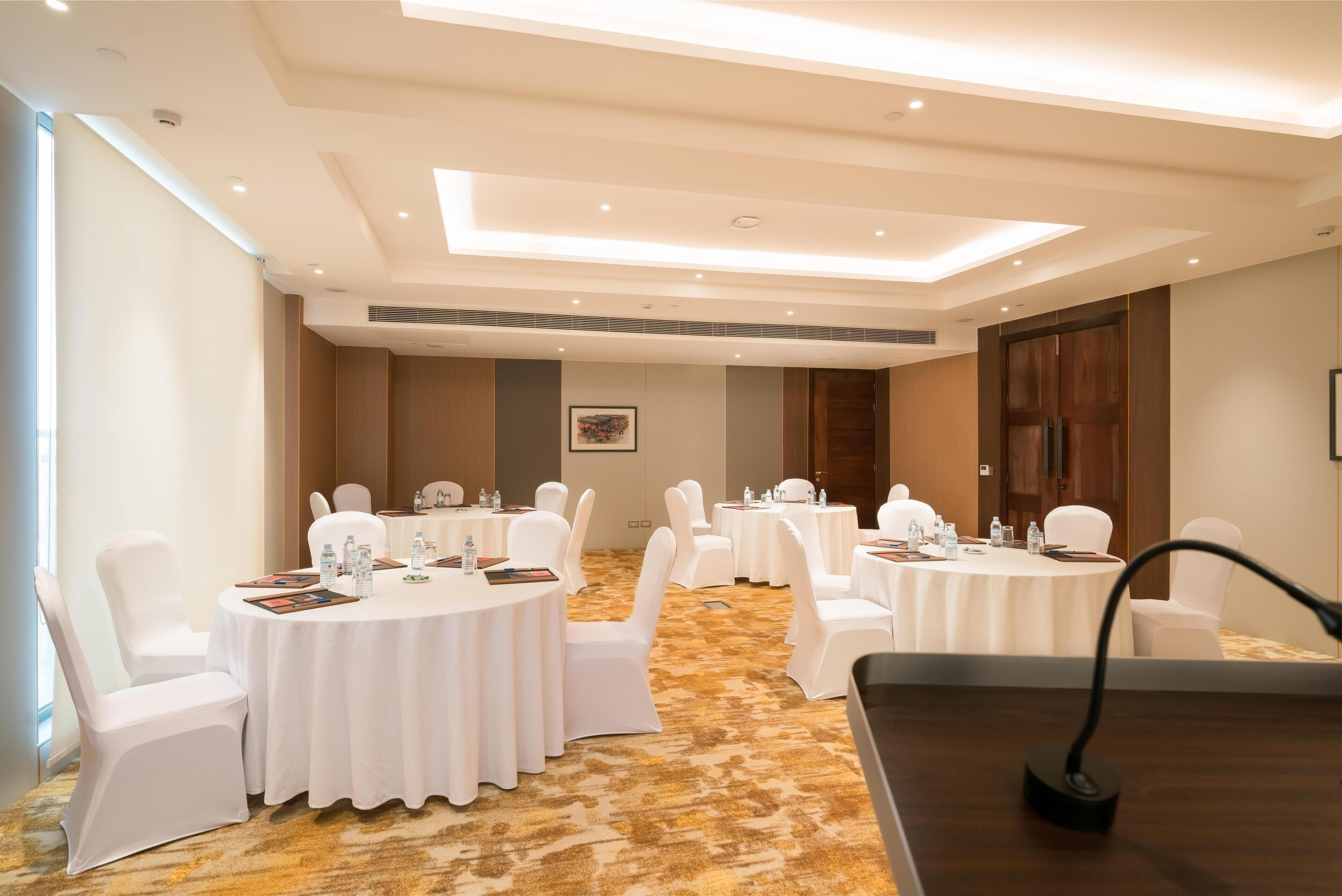 Una sala de conferències amb taules rodones, cadirees blanques i un sòl amb moqueta.