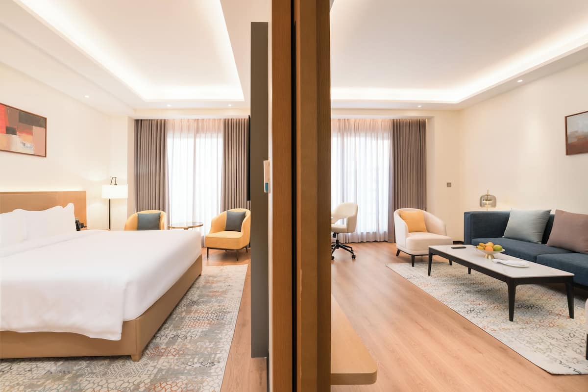 A hotel room with a bed, two armchairs, a sofa, a coffee table, and a desk.