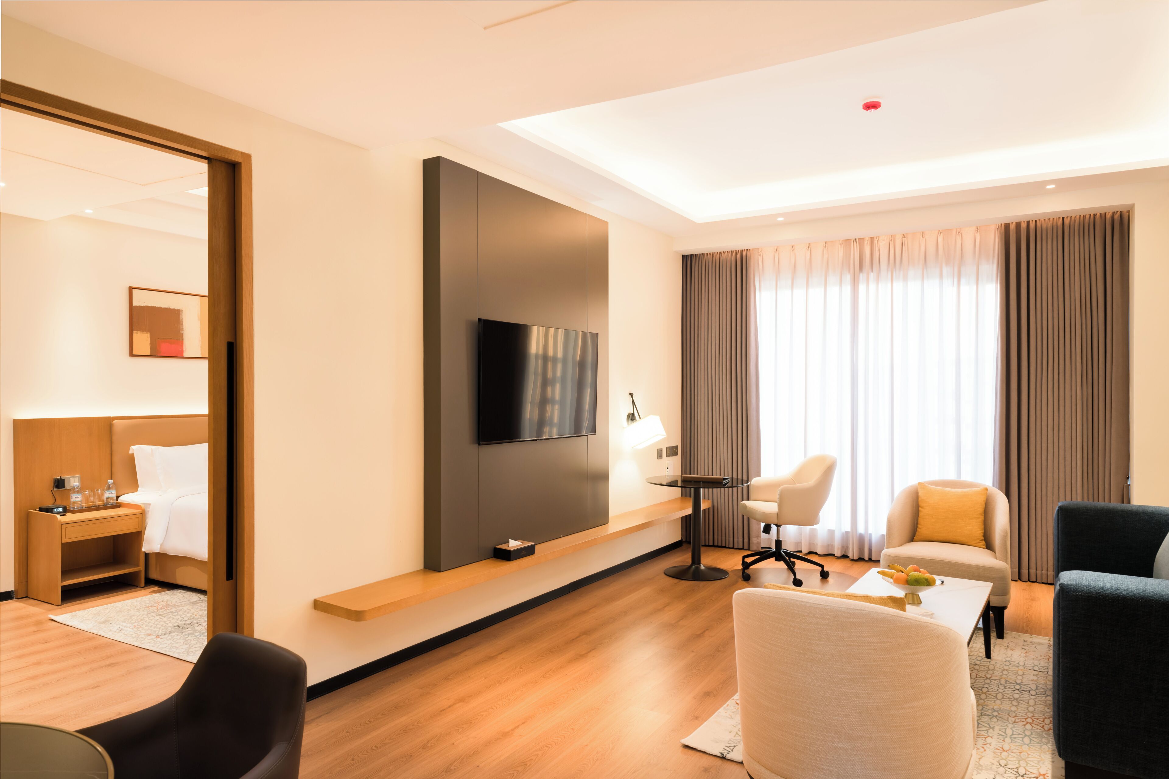 A modern hotel room with a flat-screen TV, a sofa, a chair, a desk, and a bed.
