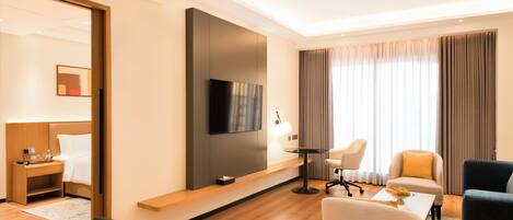A modern hotel room with a flat-screen TV, a sofa, a chair, a desk, and a bed.