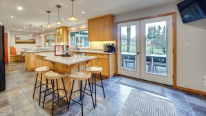 Una cocina moderna con una isla central, taburetes de bar, armarios de madera y un ventanal con vistas a una terraza.