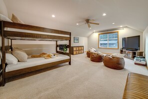 Une chambre avec un lit superposé, des fauteuils en forme de poire, un ventilateur de plafond et un téléviseur.