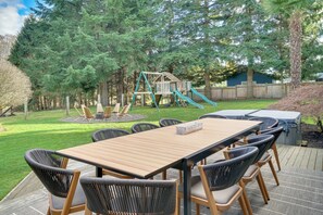 Une terrasse en bois avec une table et des chaises, entourée d’une cour verdoyante et d’une clôture en bois.