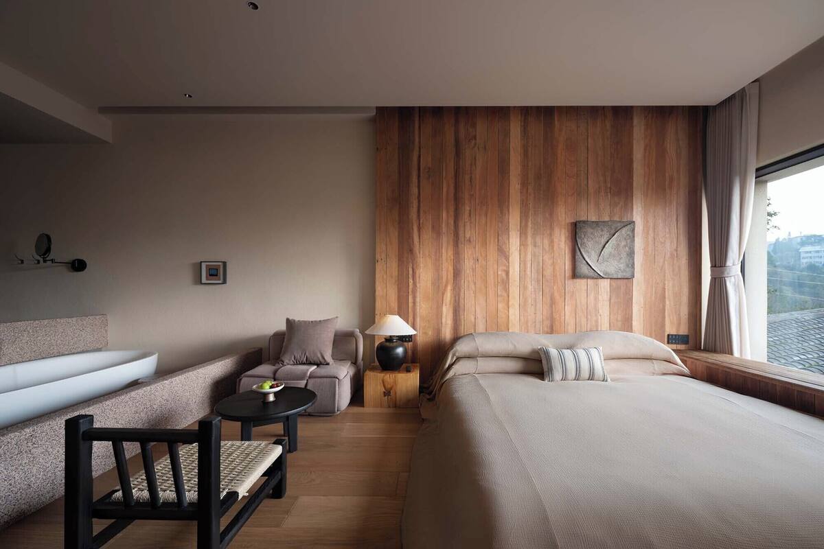 Una habitación de hotel moderna con una cama grande, un sofá, una mesita y una silla.