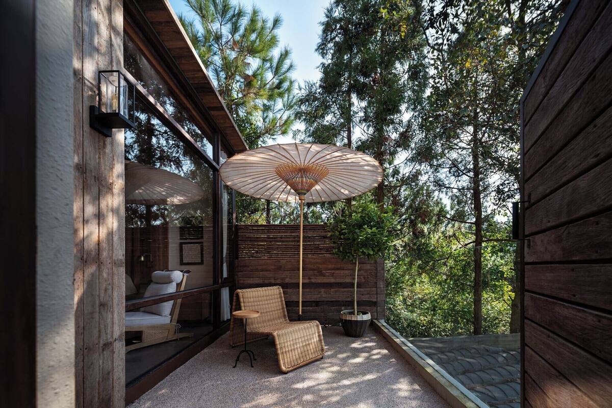 Un espacio al aire libre moderno con una silla de mimbre, una mesita redonda y un paraguas grande.