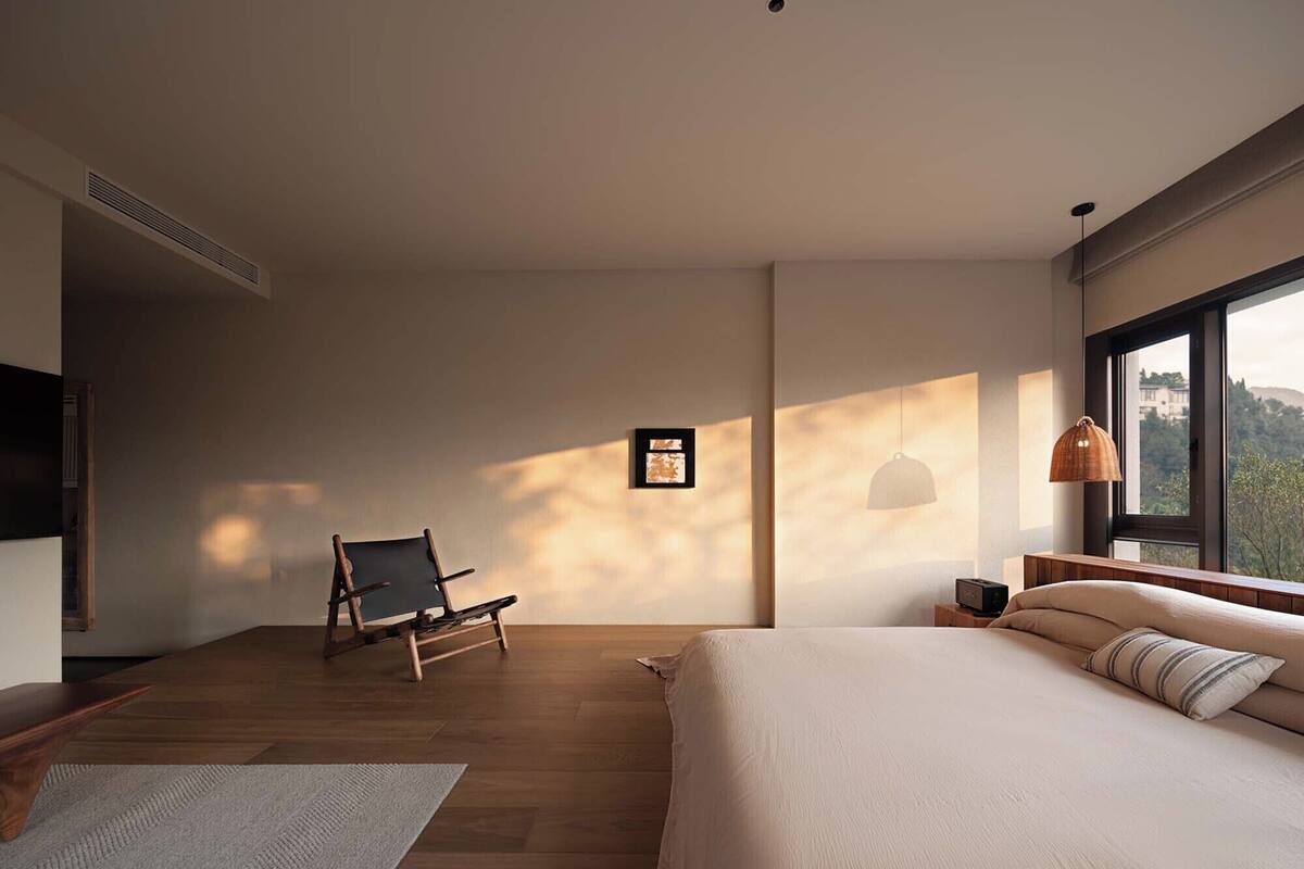Un dormitorio moderno con una cama grande, una silla, una mesita de noche y vistas al exterior a través de una ventana.
