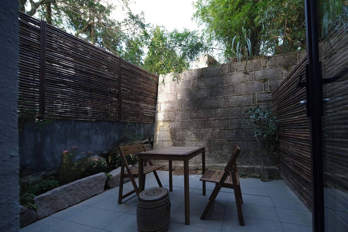 Un patio con una mesa y sillas, un taburete tejido y un muro de piedra.