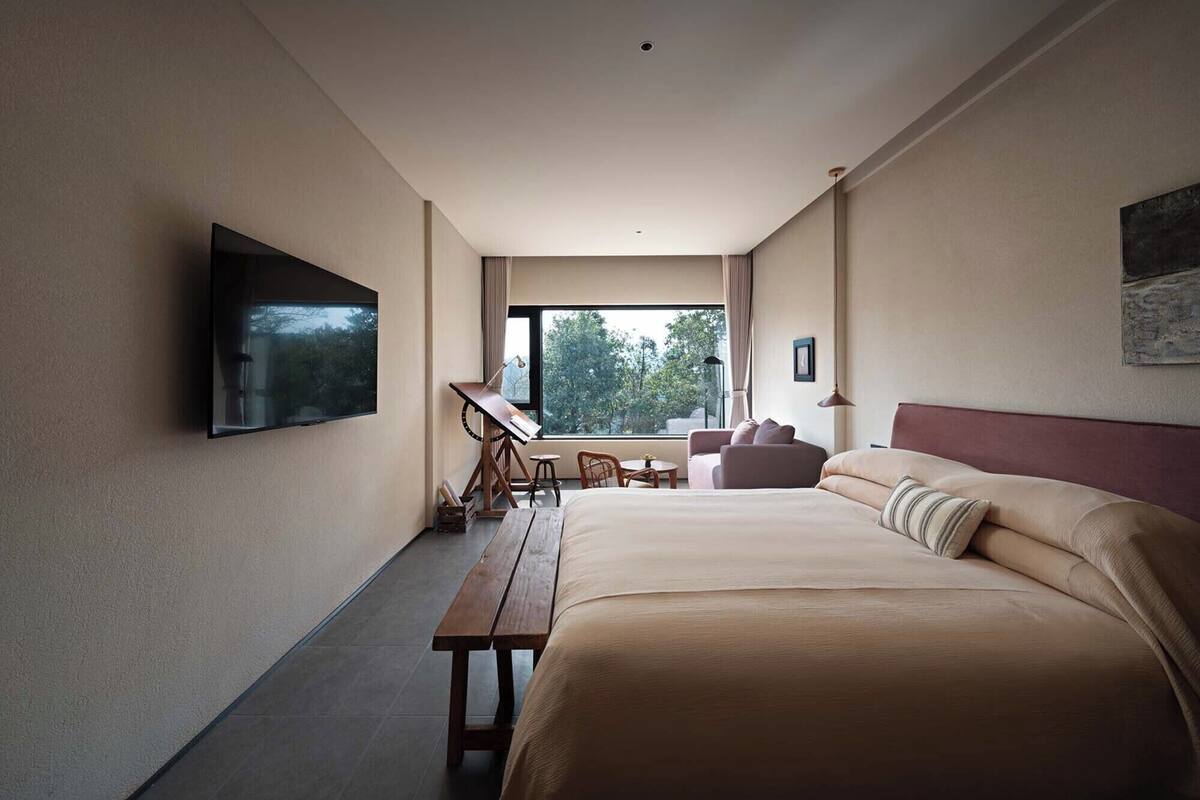 Un hotel moderno con una cama grande, un televisor de pantalla plana en la pared, un escritorio con una silla y vistas a árboles por la ventana.
