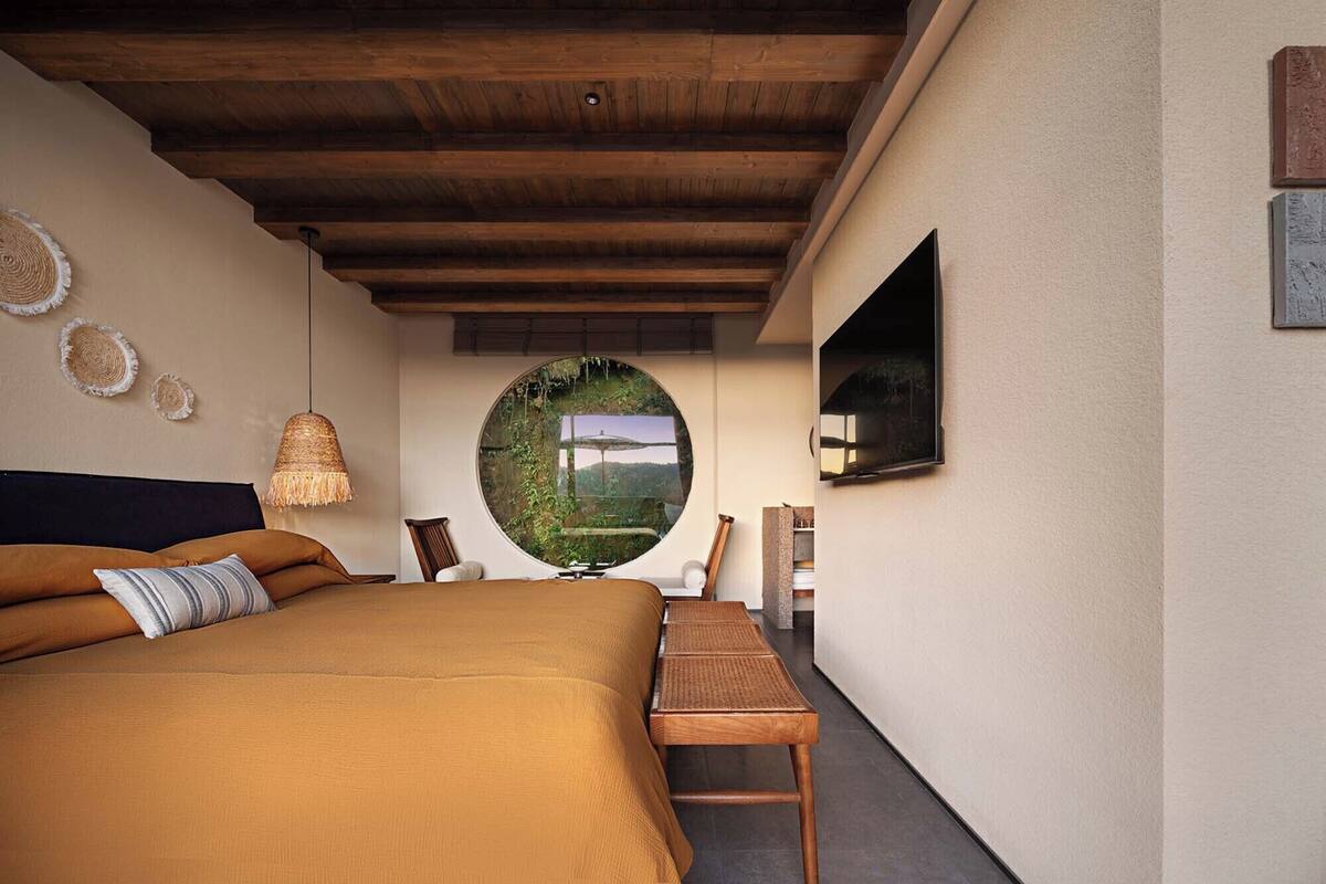 Un dormitorio con una cama grande, un ventanal redondo, un televisor y una mesita.