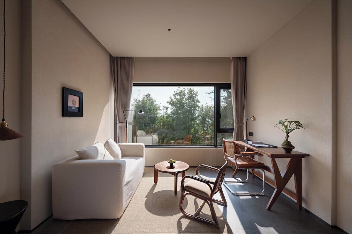Una habitación moderna y luminosa con un gran ventanal, un sofá, una mesa de comedor y una pequeña planta.