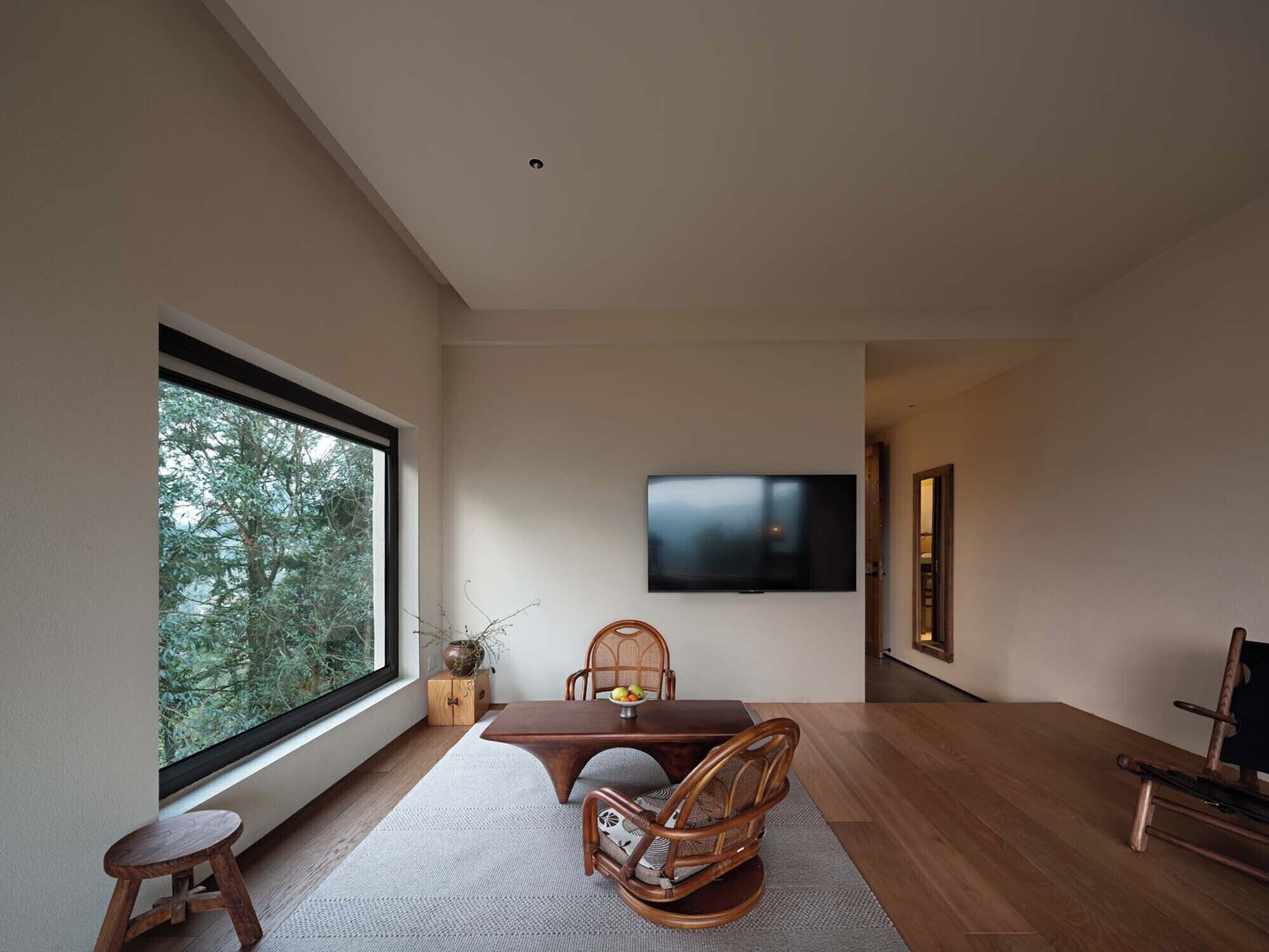 Una sala de estar moderna con un ventanal grande, un televisor de pantalla plana montado en la pared, una mesa de comedor con sillas y un taburete pequeño.