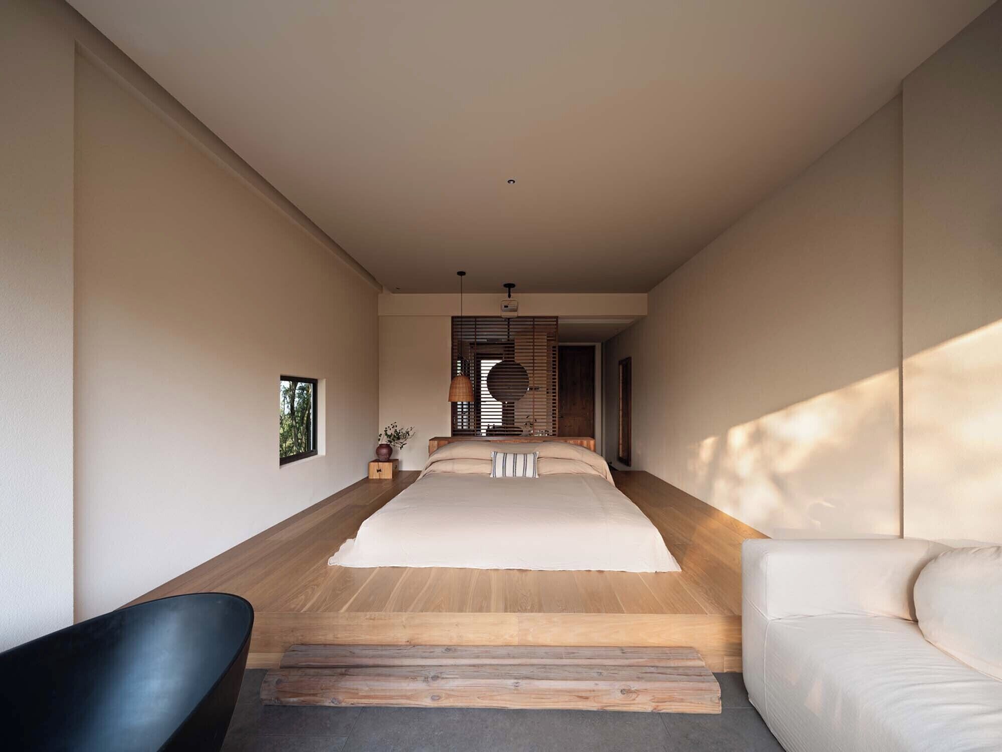 A modern bedroom with a large bed, a wooden floor, a black chair, and a white sofa.