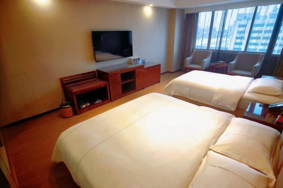 A hotel room with two beds, a TV, a desk, and a window with a city view.