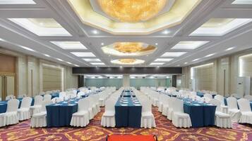A banquet hall with rows of tables, white chairs, and a red carpet.