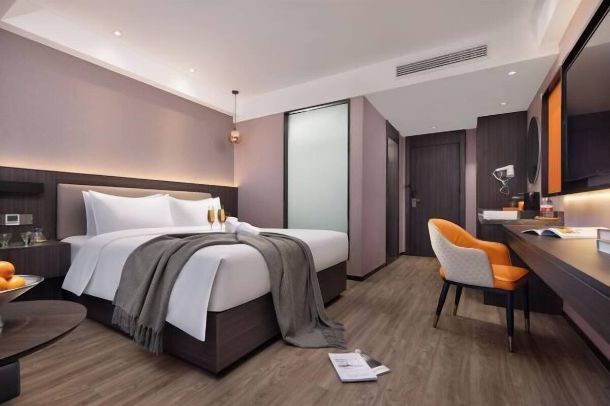 A modern hotel room with a bed, bedside table, chair, and a desk with a chair.