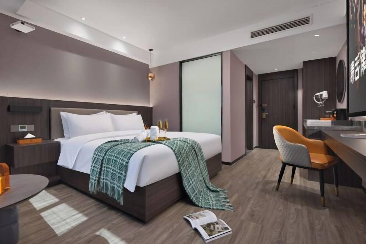 A modern hotel room with a bed, bedside table, chair, desk, and a large mirror.