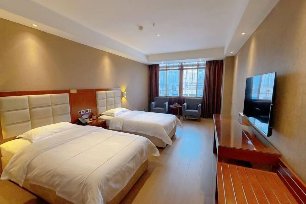 A hotel room with two beds, a TV, a desk, and a window with curtains.