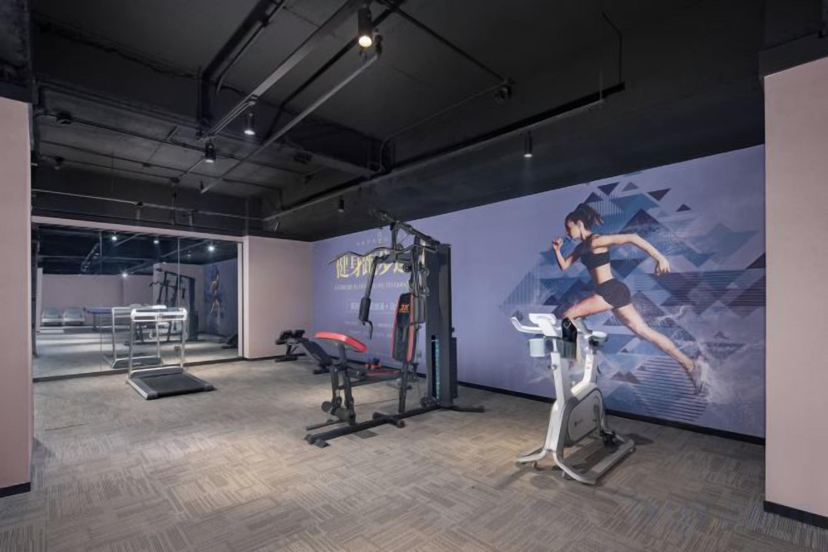 Un gimnasio con equipamiento de ejercicio, una pared con diseño geométrico y un ventanal grande.