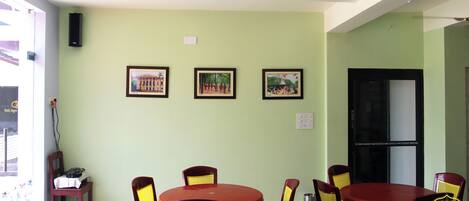Zona pranzo con tavoli rossi e sedie gialle, quadri appesi al muro e una porta nera.