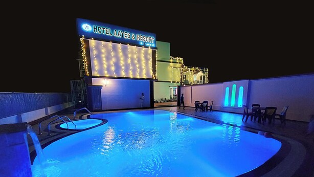A hotel with a pool area, a sign reading "HOTEL AAYES & RESORT," and a building with illuminated string lights. - Hotel Aayes & Resort (Bolpur)