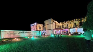 A hotel with a well-lit exterior, a visible signboard, and a grassy lawn area. - Hotel Aayes & Resort (Bolpur)
