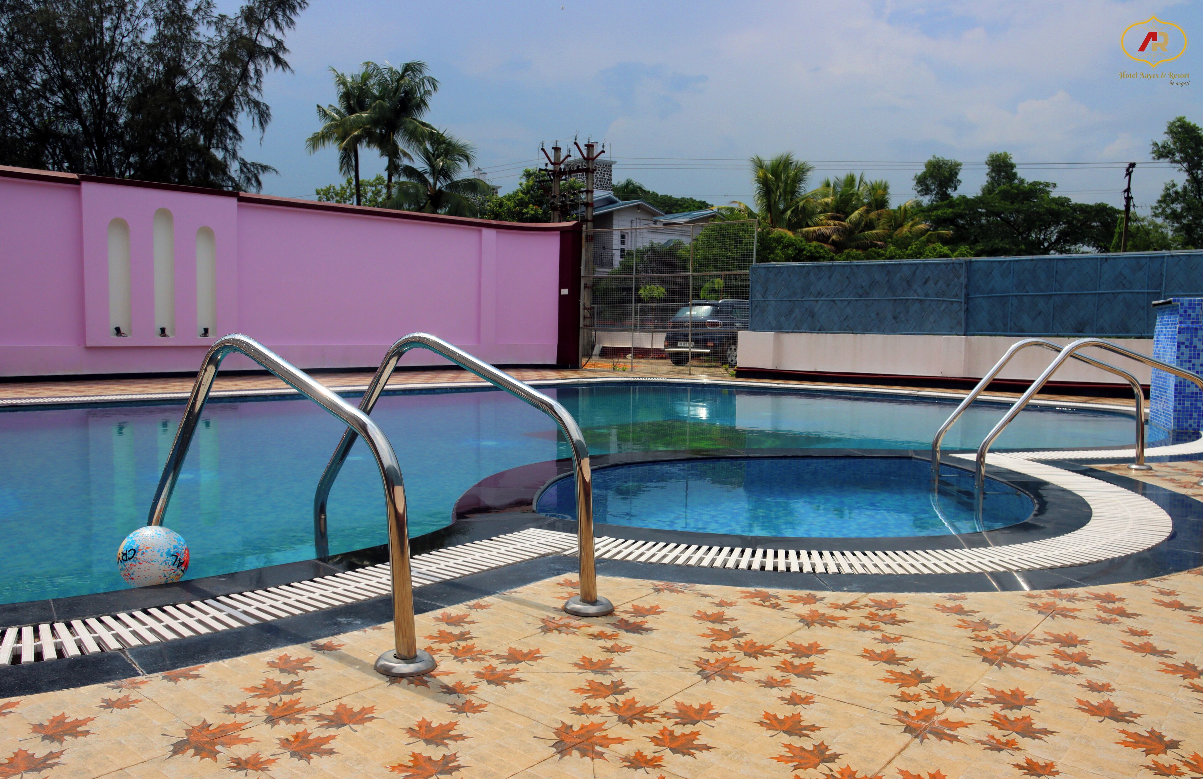 A swimming pool with metal ladders, surrounded by a tiled deck with a leaf pattern.