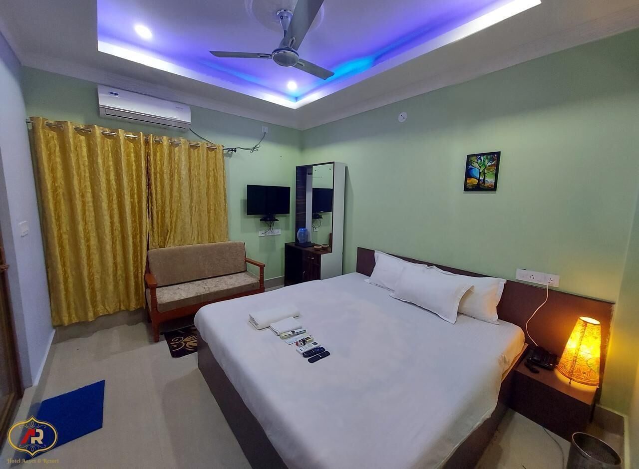 A hotel room with a bed, a chair, a desk, a mirror, and a ceiling fan.