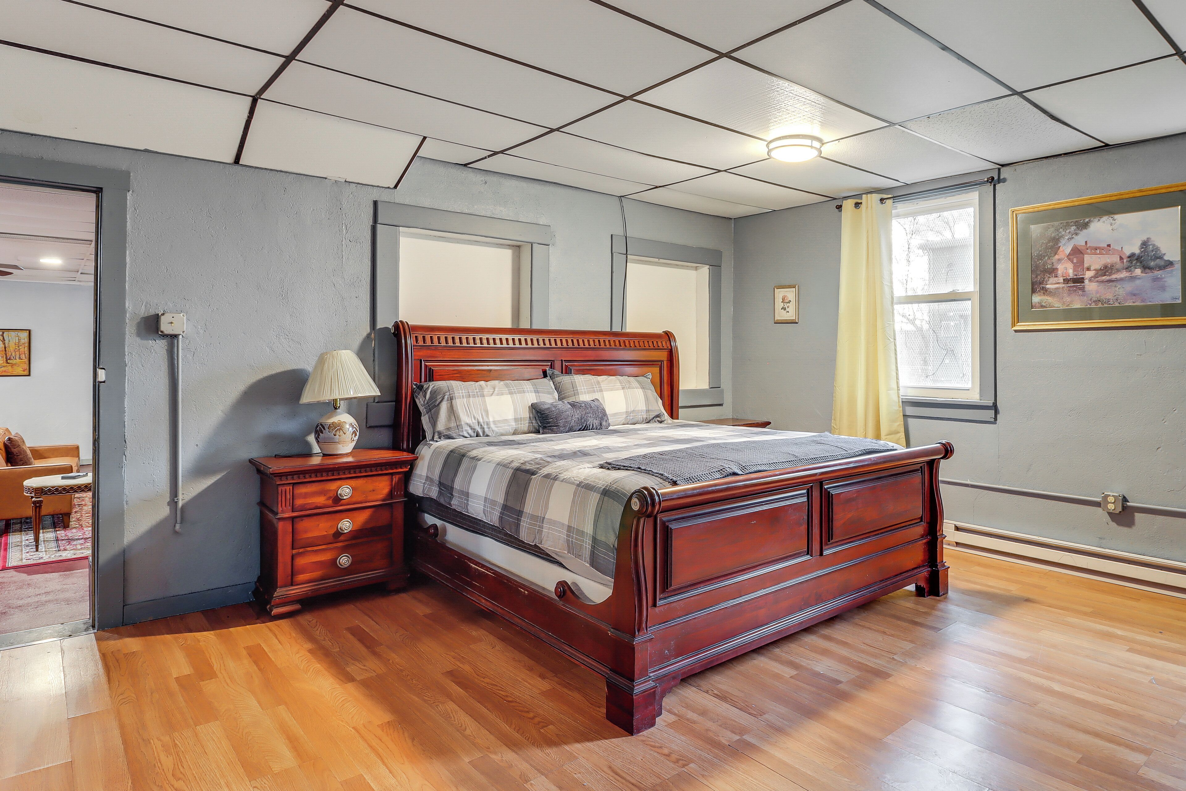 Un dormitorio con una cama de madera, una mesita de noche, un armario y una ventana con cortina.