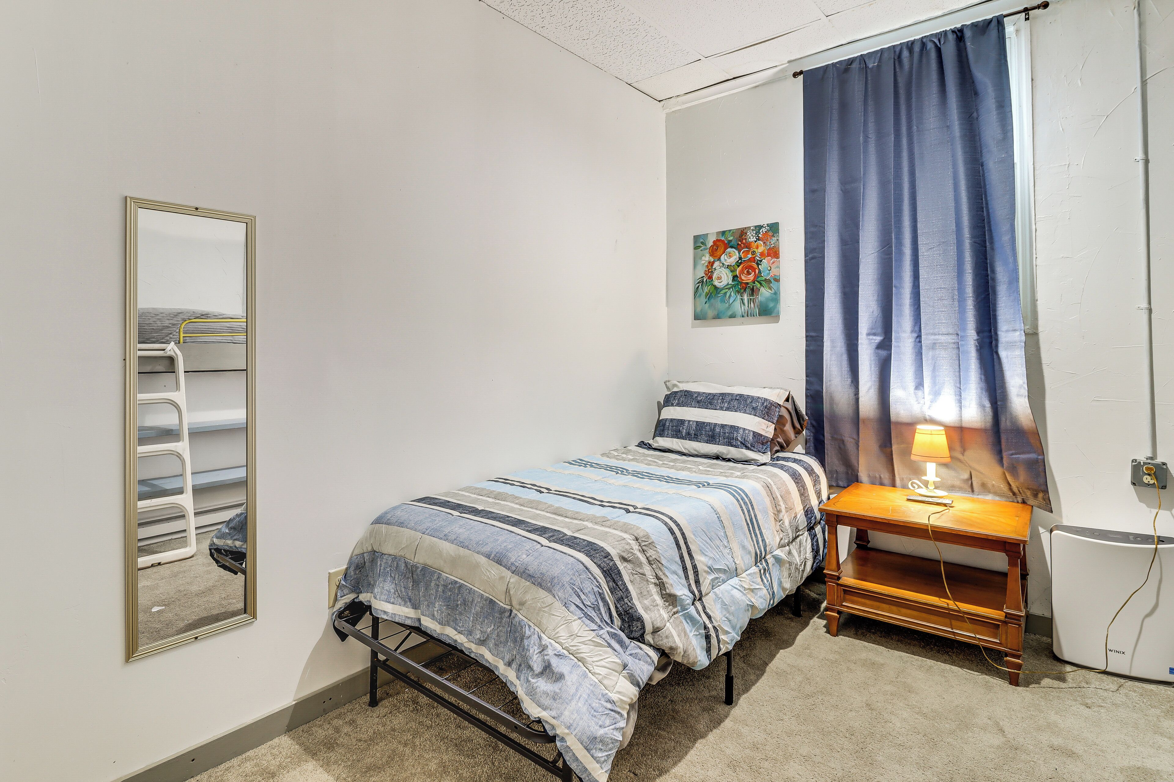 Un dormitorio con cama, una mesita de noche con lámpara, un espejo y un cuadro en la pared.