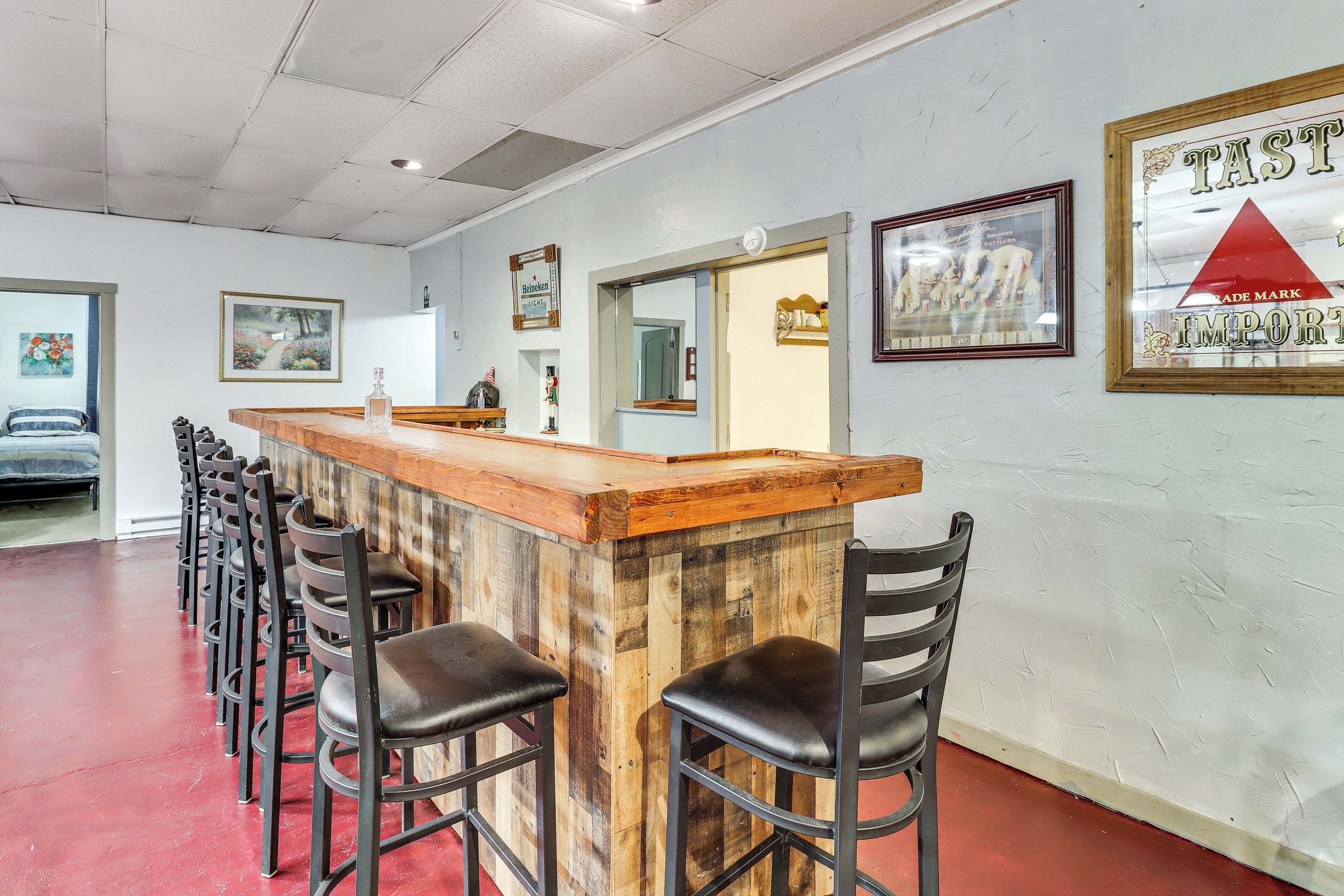 A bar area with a wooden counter and black bar stools, framed pictures on the walls, and a red floor.