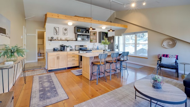 Una cocina moderna con vigas de madera, una isla central con taburetes de bar y un comedor con una mesa redonda.
