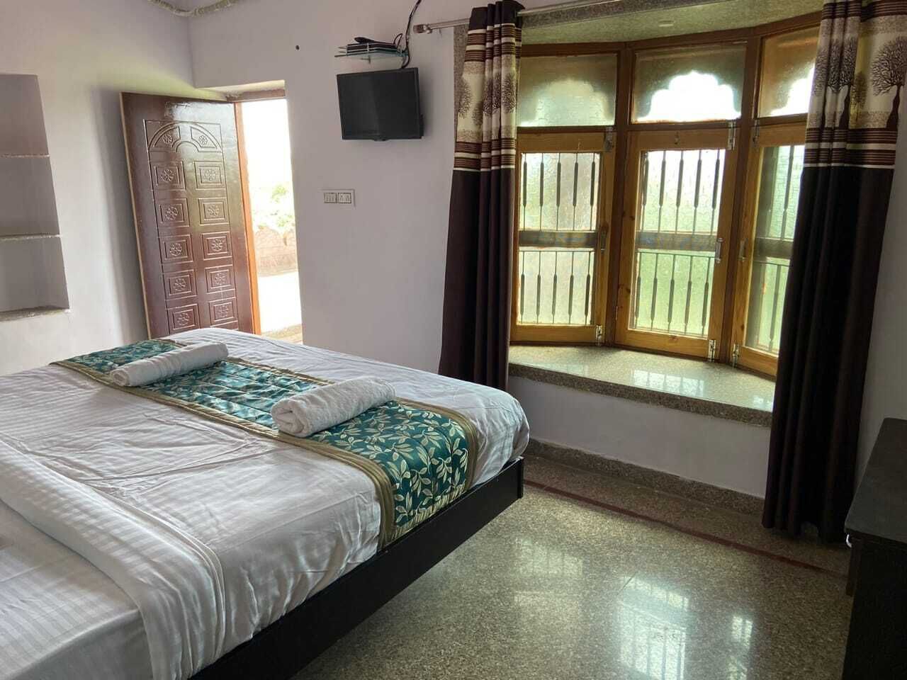 A bedroom with a bed, a television, a window with curtains, and a door.