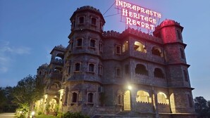 A large, historic building with multiple levels and arched windows, illuminated by warm lighting. - Indraprasth Heritage Resort (Gogunda)