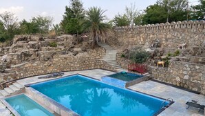 A swimming pool with stone walls and a staircase leading up to a higher level. - Indraprasth Heritage Resort (Gogunda)