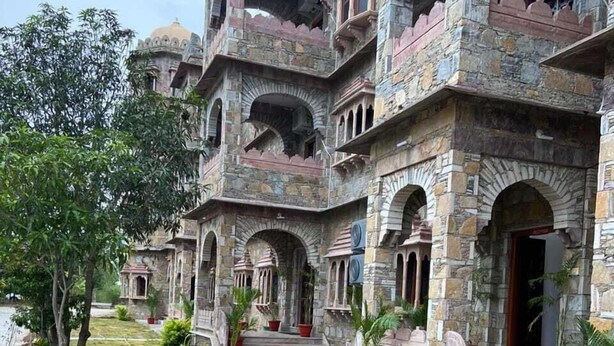 A historic building with multiple balconies and arched windows, surrounded by a well-maintained lawn and potted plants. - Indraprasth Heritage Resort (Gogunda)