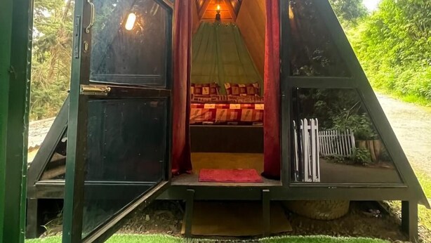 Une structure triangulaire en forme de tente, avec un lit à l’intérieur, une porte et un petit espace servant de porche.