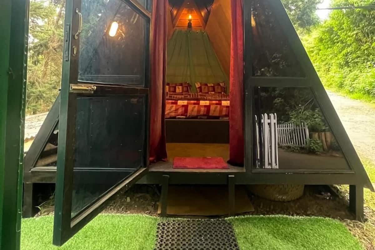 A triangular tent-like structure with a bed inside, a door, and a small porch area.