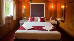 Une chambre aux murs lambrés, avec un grand lit, des tables de chevet, une fenêtre et des lampes fixées au mur.