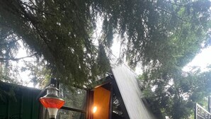 Une petite cabane d’une seule pièce, avec un toit en pente, un rideau rouge et une lampe allumée à l’extérieur.