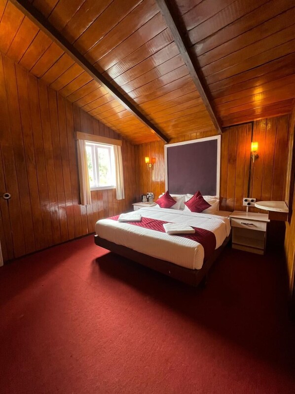 Quarto com painéis de madeira, uma cama grande, uma mesa de cabeceira e uma janela.