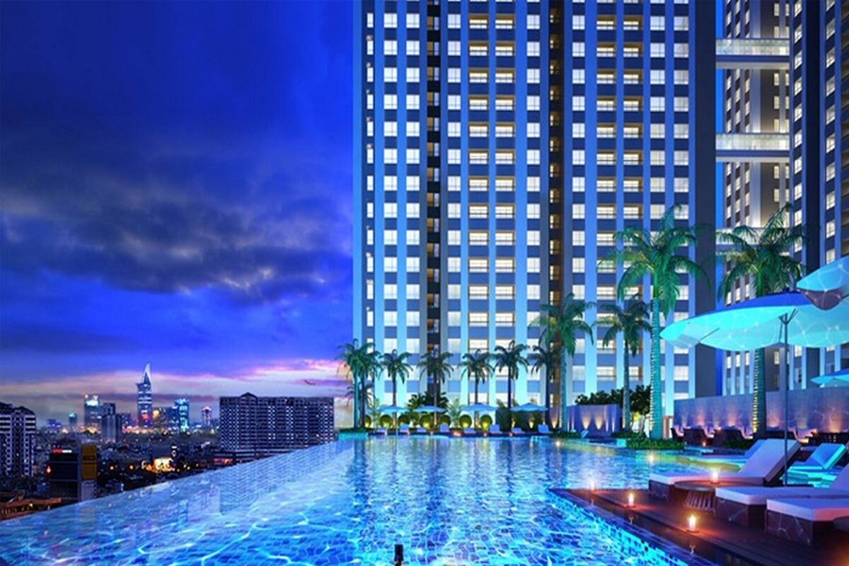 A modern hotel with a rooftop infinity pool, palm trees, and a city skyline at dusk.