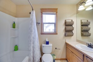 Ein Badezimmer mit Toilette, Waschbecken, Spiegel, Fenster und Duschvorhang.