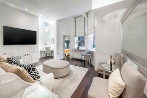 A modern living room with a flat-screen TV, a round ottoman, and a sofa with patterned cushions. - Hans Place Residences (London)