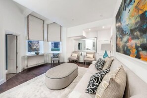 A modern living room with a sofa, ottoman, and a large abstract painting. - Hans Place Residences (London)