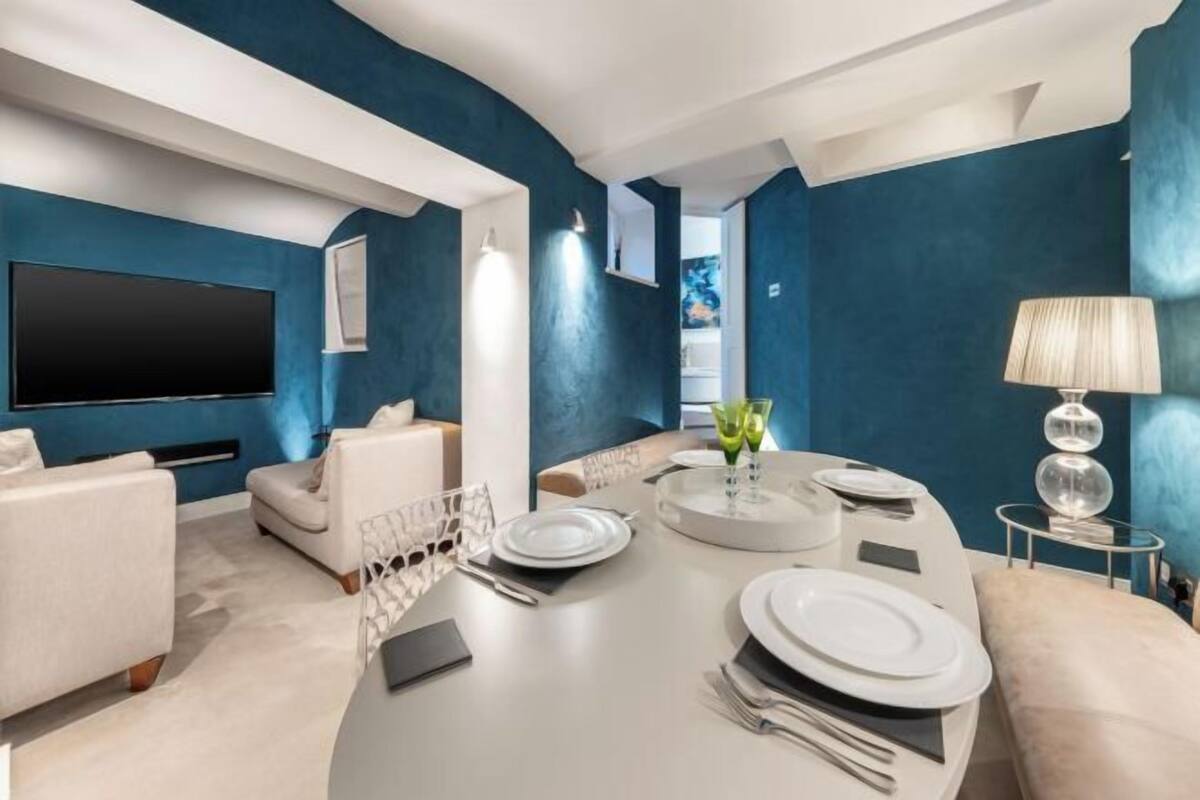 Ein modernes Wohnzimmer mit Fernseher, Sitzgelegenheiten, einem Esstisch für vier Personen und einer blauen Akzentwand.
